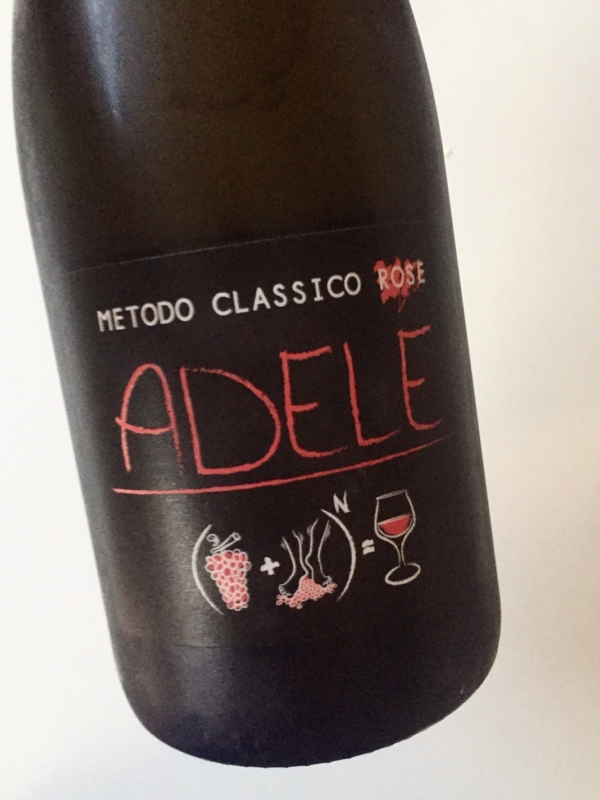 Bottiglia scura, il nome del vino sembra scritto con un pennarello rosso, Adele, in onore della figlia del vignaiolo. L'immagine è semplice, con dei simboli disegnati, un'addizione, l'uva ed il vignaiolo tra cui viene messo il più, danno il vino.