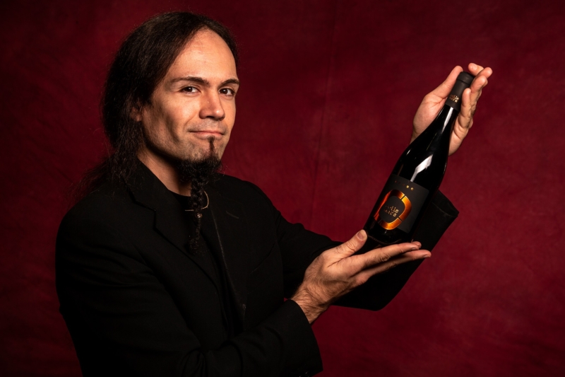 vini marchigiani Daniele Sartori, in look total black su sfondo rosso, mostra una delle bottiglie della collezione Collemara